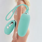 Dressed in white lingerie, a person holds the elegant VeDO Kiwi Bullet - Turquoise, its turquoise color enhanced by metallic details. This rechargeable bullet from VeDO features multiple vibration modes, making it pop against the simple white background.